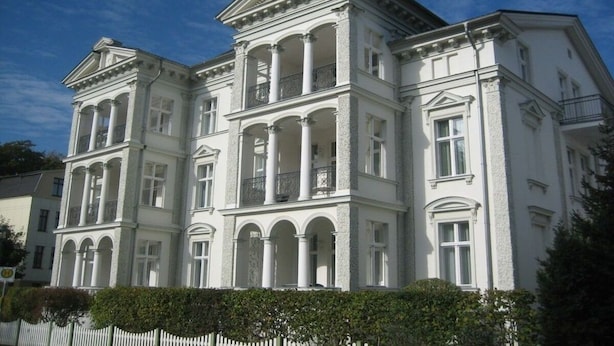 Un grande edificio neoclassico, bianco, con diversi piani e balconi.