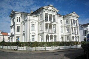 Um edifício grande, branco e de estilo clássico, com vários andares e fachada simétrica.