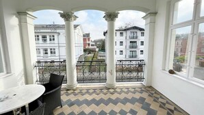 Un balcone con pavimento a scacchi, colonne bianche e vista sugli edifici circostanti.