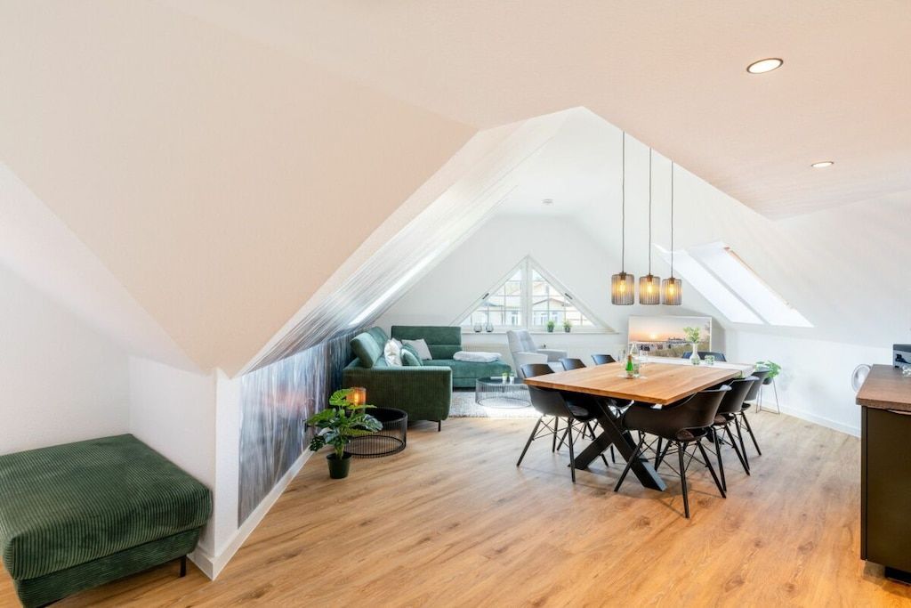 A spacious loft with a dining area, a green sofa, and a view of the city through large windows.