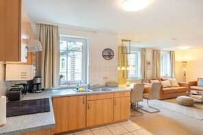 A modern kitchen with a built-in island, a dining area with a sofa, and a living room with a coffee table. - House at Buchenpark 11 (Heringsdorf (Seebad))