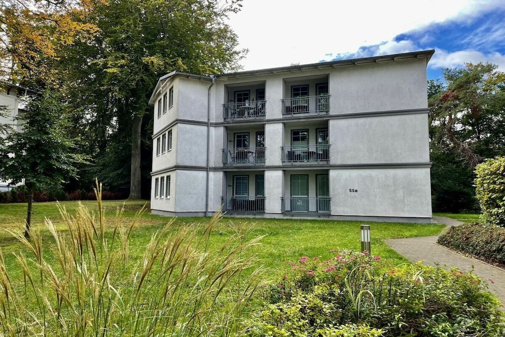 A multi-story building with balconies, surrounded by greenery and trees.