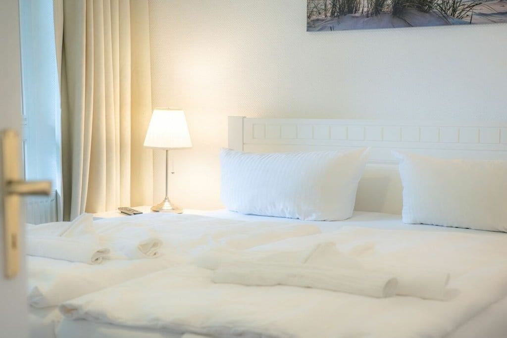 A hotel room with a neatly made bed, a bedside lamp, and a painting on the wall.