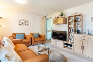 Ein modernes Wohnzimmer mit einer Couch, Sesseln, einem Couchtisch, einem Flachbildfernseher und Einbauschränken.
