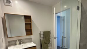 Un bany modern amb plat de dutxa de vidre, un lavabo amb mirall i un escurapins.