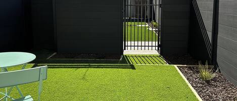 A gated courtyard with artificial grass, a metal gate, and a small table with a chair.