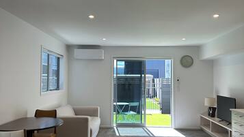 A modern living room with a sofa, a dining table, and chairs. There is a sliding glass door leading to a balcony.
