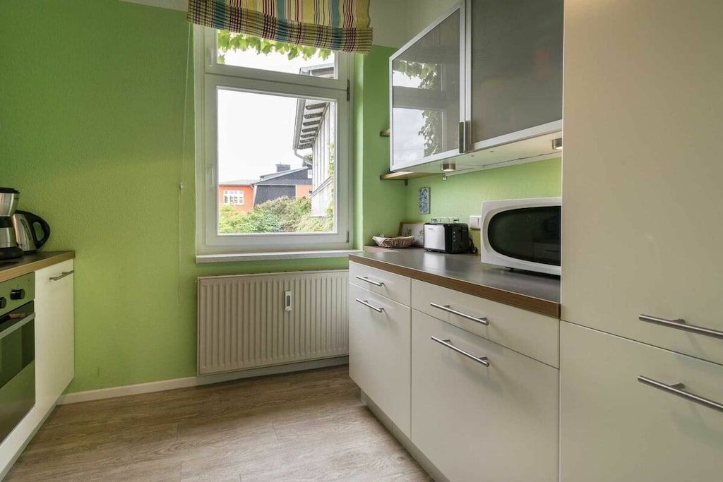 A kitchen with a window, white cabinets, a microwave, and a kettle.