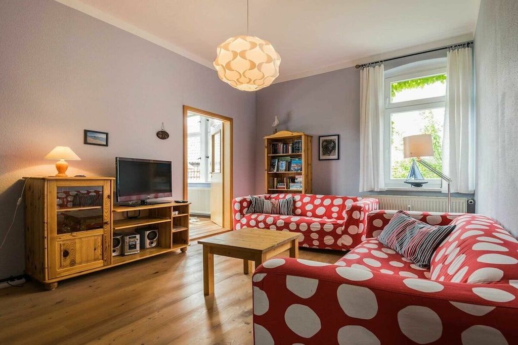 A living room with a television, wooden cabinet, red polka-dotted sofa, and a wooden coffee table.