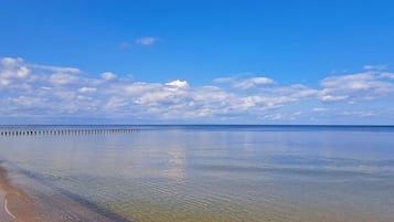 A calm beach with clear water and a wooden pier extending into the sea.