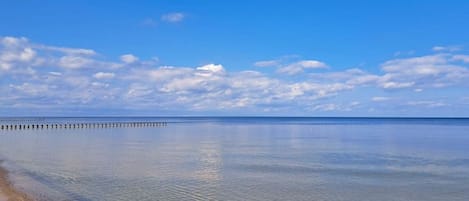 Una playa tranquila con aguas cristalinas y un muelle de madera que se adentra en el mar.