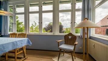 A room with a dining table, chairs, a lamp, and large windows with curtains.