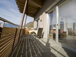 A balcony with a view of mountains, a table with chairs, and a glass door leading to an interior space. - "red" on the Sandwiesen Farm (Gargazzone)