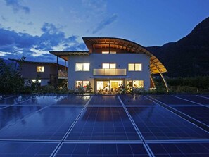 A modern two-story building with a flat roof and a curved extension, surrounded by solar panels. - "red" on the Sandwiesen Farm (Gargazzone)