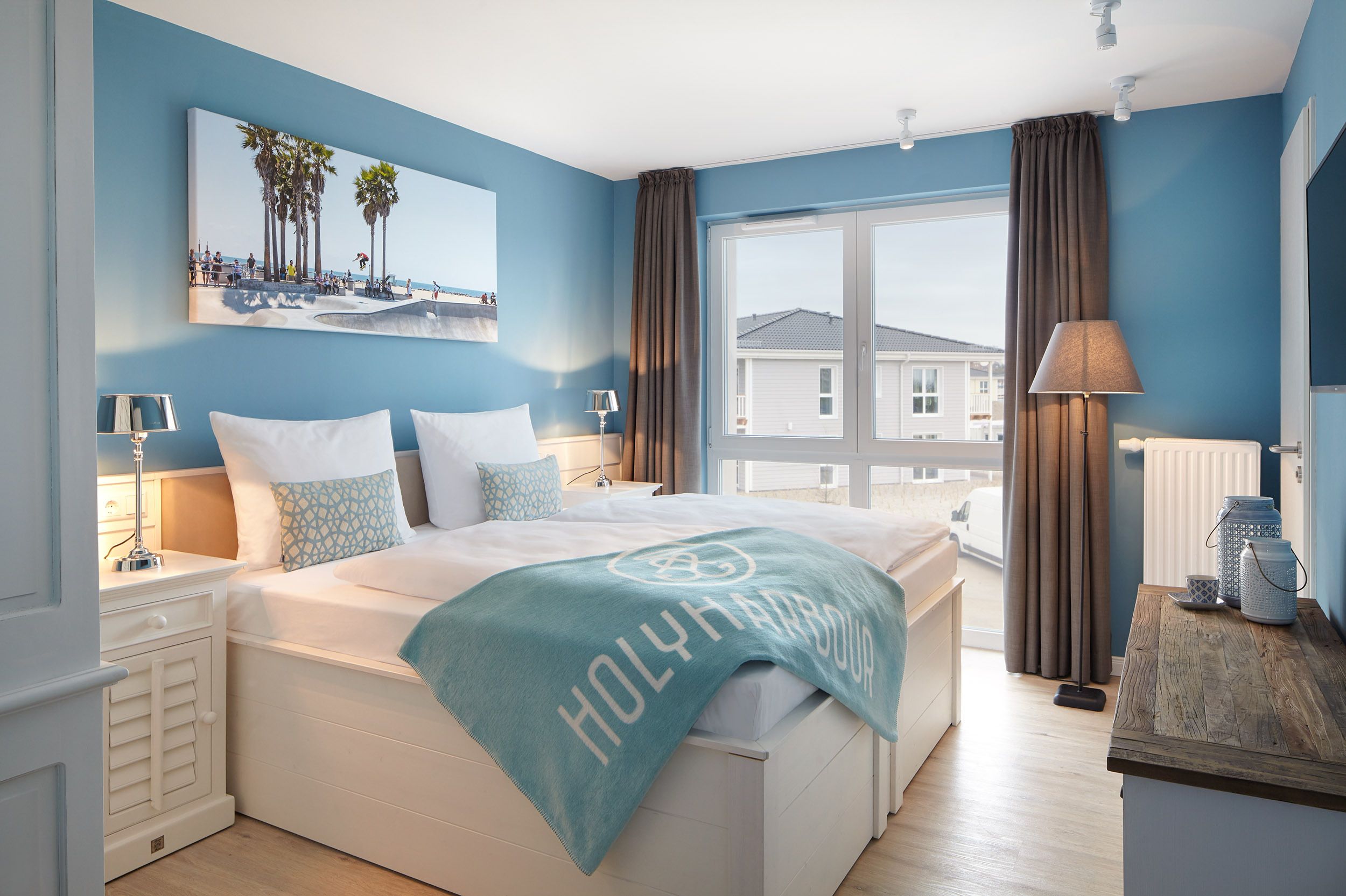 Un dormitorio con una cama grande, vistas al mar y una escena de playa en la pared.
