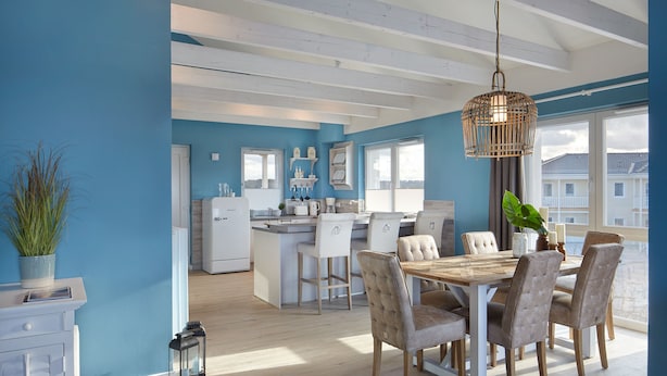 A modern kitchen with a central island, white cabinetry, and a dining area with a wooden table and upholstered chairs. - Vrbo Property (Heiligenhafen)