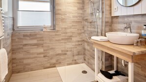 A modern bathroom with a wooden floor, a glass shower enclosure, a white sink, and a mirror above it. - Vrbo Property (Heiligenhafen)