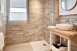 A modern bathroom with a wooden floor, a glass shower enclosure, a white sink, and a mirror above it. - Vrbo Property (Heiligenhafen)