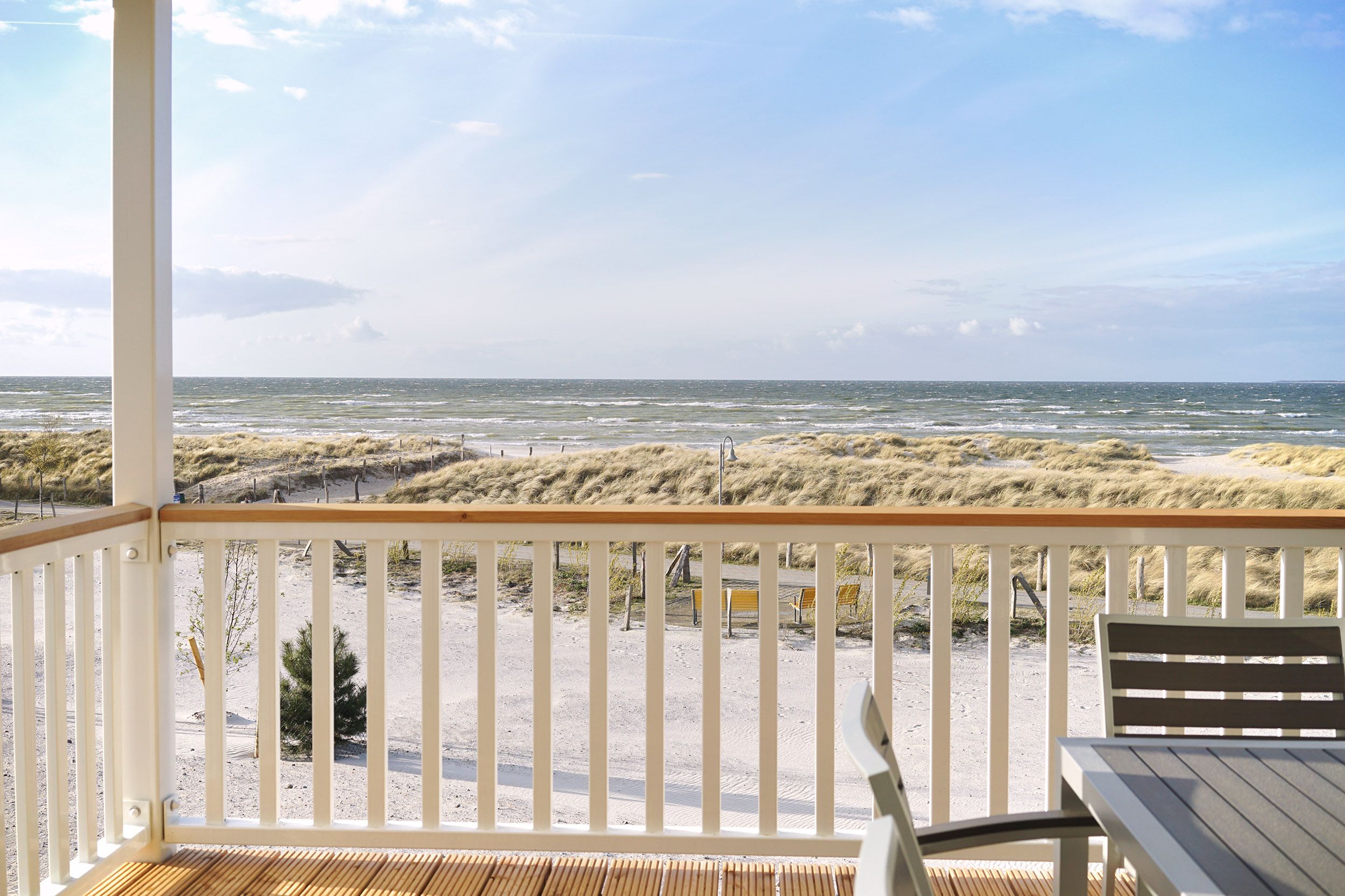 Vista a la playa desde una terraza techada con barandilla de madera, una mesa y un banco.