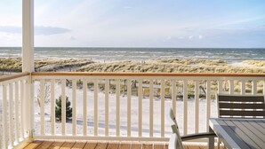 A beach view from a covered deck with a wooden railing, a table, and a bench. - Vrbo Property (Heiligenhafen)