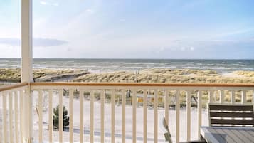 Vista a la playa desde una terraza techada con barandilla de madera, una mesa y un banco.