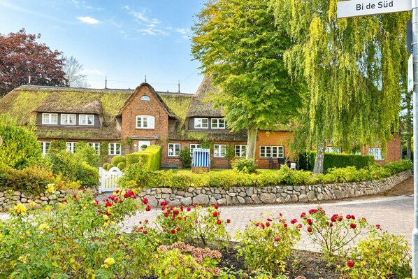 Ein traditionelles Haus mit einem Reetdach, umgeben von einem gepflegten Garten mit verschiedenen Pflanzen und Blumen.