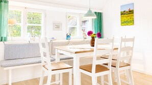 Un comedor luminoso con una mesa de madera, sillas blancas, un banco a rayas y una lámpara colgante.