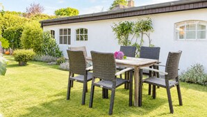 Un patio con mesa y sillas, rodeado por un césped y jardín bien cuidados.