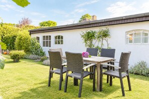 Eine Terrasse mit Tisch und Stühlen, umgeben von einem gepflegten Rasen und Garten.