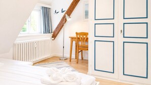 Un dormitorio con techo inclinado, una silla de madera, una mesita de noche y un radiador.