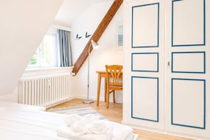 Ein Schlafzimmer mit schrägem Dach, einem Holzstuhl, einem Nachttisch und einer Heizung.