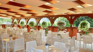 Un área de comedor al aire libre con mobiliario de mimbre blanco y una estructura de techo de madera.