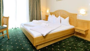 Una habitación de hotel con una cama de madera, una silla, una mesita de noche y una lámpara fijada a la pared.