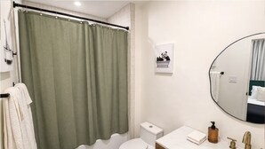 Casa de banho com cortina de chuveiro verde, sanita branca e lavatório com espelho.