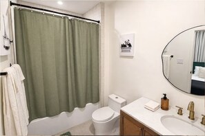 A bathroom with a green shower curtain, white toilet, and a sink with a mirror. - King Bed-Unbeatable Location-Bishop Arts- Unit 3 (Dallas)