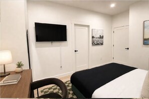 A hotel room with a bed, a desk with a lamp, a television, and two doors. - King Bed-Unbeatable Location-Bishop Arts- Unit 3 (Dallas)