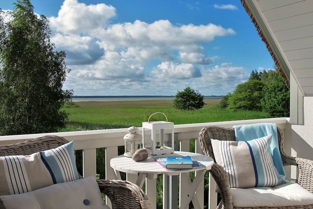 Un balcone con mobili in vimini, un tavolino e vista su un campo verde e il cielo.
