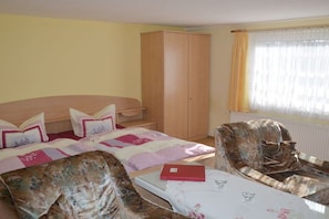 A bedroom with a bed, a wardrobe, a chair, a table, and a window with curtains. - Holiday rooms with 0 bedrooms (Kölpinsee)