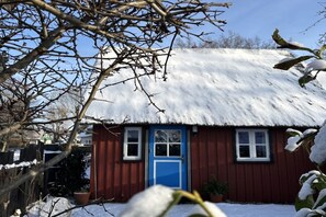A red wooden house with a blue door, surrounded by snow-covered ground and bare trees. - Holiday home in Born with swimming pool (Born)