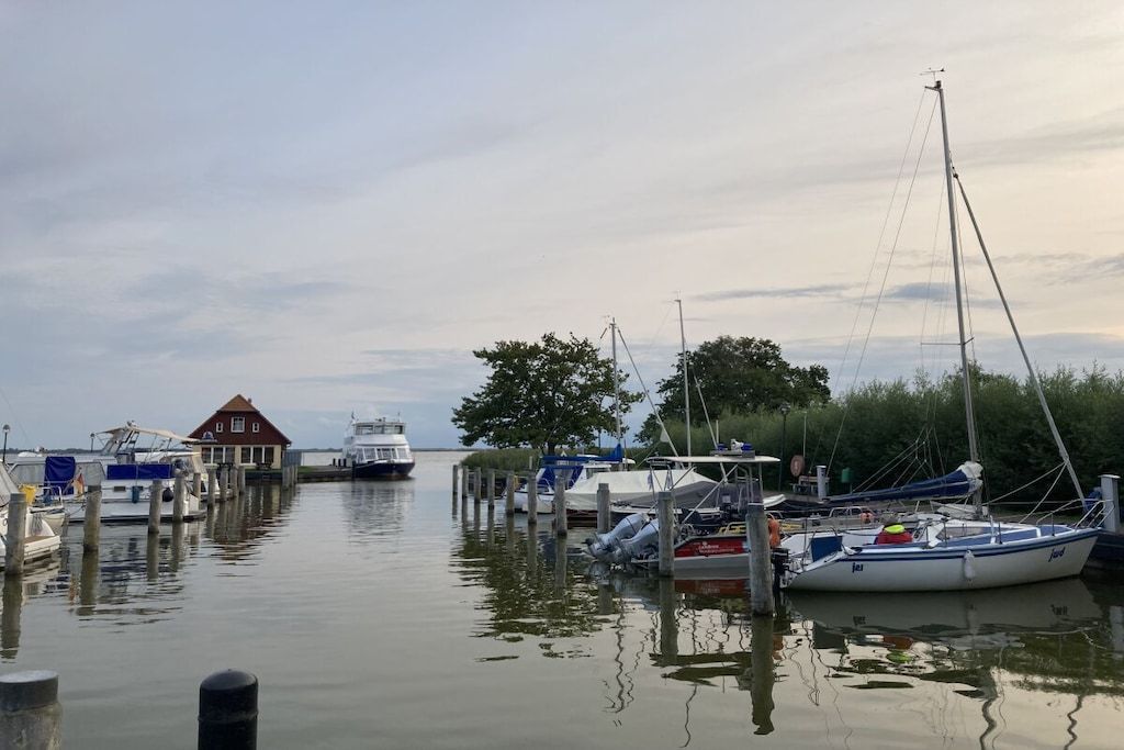 A marina with boats docked, a building with a red roof, and calm water reflecting the sky.