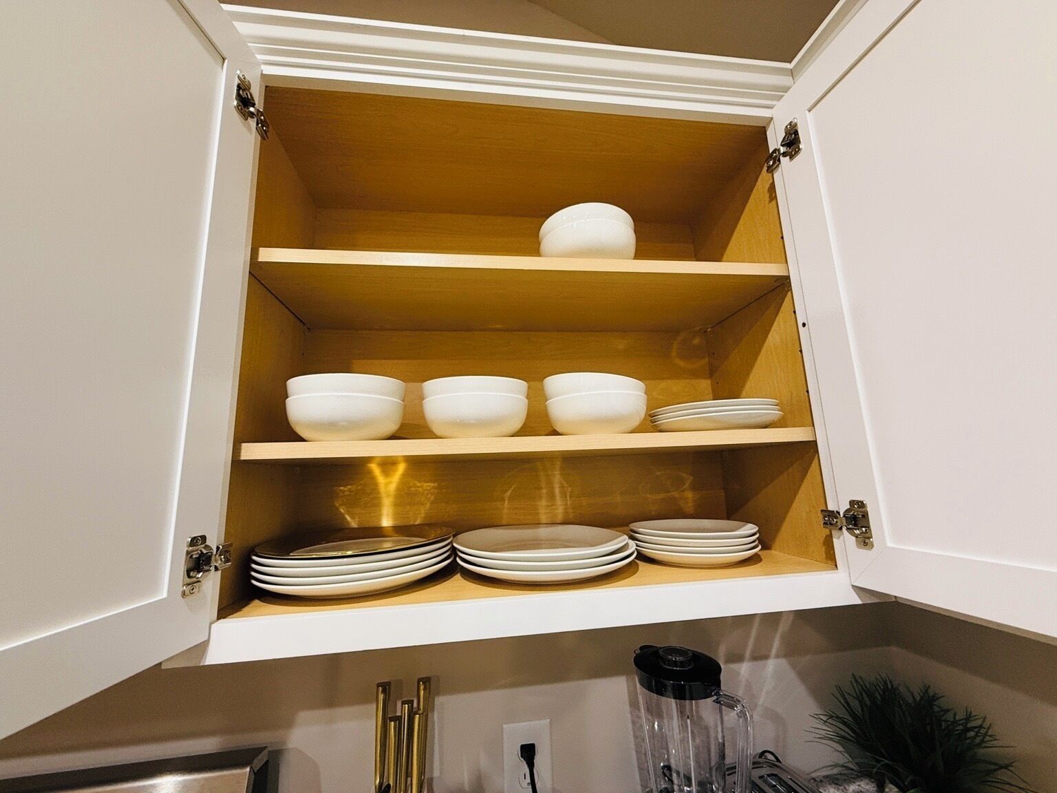A kitchen cabinet with multiple shelves holding white bowls and plates.