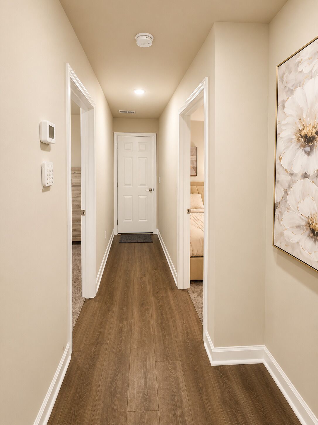 A hallway with a wooden floor, white walls, and a door at the end.