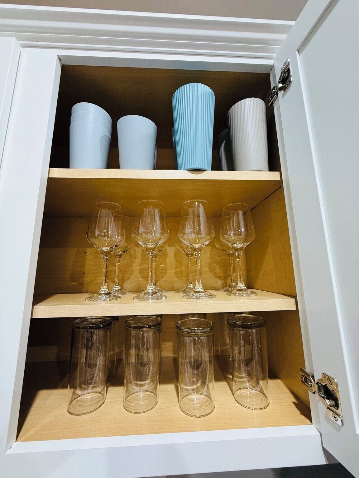 A cabinet with three shelves; the top shelf holds decorative vases, the middle shelf contains wine glasses, and the bottom shelf has empty glass tumblers.