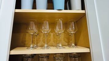 A cabinet with three shelves; the top shelf holds decorative vases, the middle shelf contains wine glasses, and the bottom shelf has empty glass tumblers.