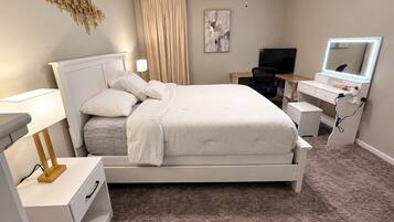 Un dormitorio con cama, mesitas de noche, escritorio, silla, ventilador de techo, televisor y espejo.