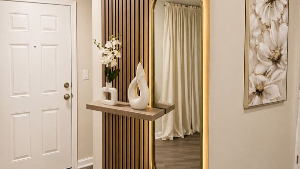 A hallway with a white door, a wall-mounted mirror, a shelf with a vase and flowers, and a framed floral artwork. - Modern Luxury 3BR Home in Cullman (Cullman)