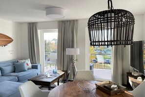 A modern living room with a sofa, coffee table, and a hanging light fixture. - Holiday apartment with 1 bedroom (Kühlungsborn)
