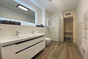Ein modernes Badezimmer mit einem Doppelwaschbecken, einer Duschkabine aus Glas und einer weißen Toilette.