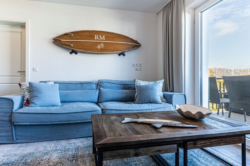 Una sala de estar con un sofá azul, una mesa de centro de madera y una decoración de pared con forma de tabla de surf.