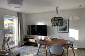 A modern living room with a flat-screen TV, a wooden dining table, and a large window. - Holiday apartment with 1 bedroom (Kühlungsborn)